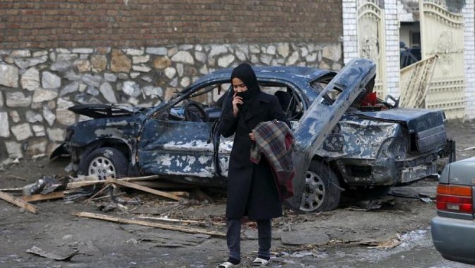 An Afghan woman walks past a damaged car after a suicide attack on French restaurant 